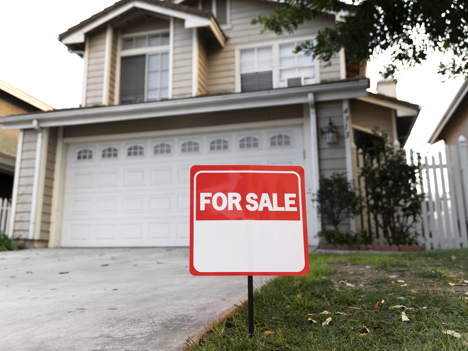 A for-sale yard sign in front of a two-story home